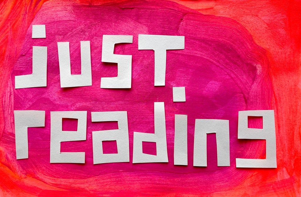A brightly painted orange and pink background with cut out paper letters spelling: just reading